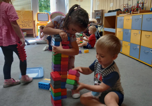 Dziewczynka z chłopcem budują wieżę z klocków.