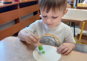 Chłopiec stempluje kropki farbą na sylwecie koła.