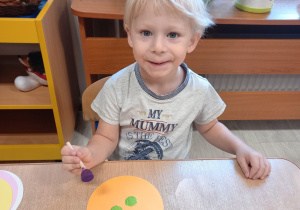 Chłopiec stempluje kropki farbą na sylwecie koła.
