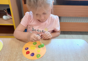Dziewczynka stempluje kropki farbą na sylwecie koła.