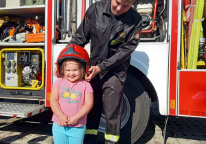 Dziewczynka w kasku strażackim i panem strażakiem.