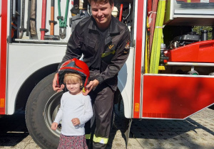 Dziewczynka w kasku strażackim i panem strażakiem.