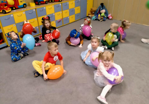 Dzieci z balonami siedzą na dywanie.
