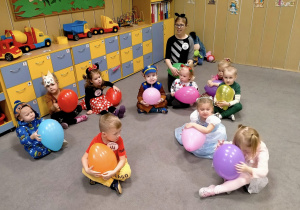 Dzieci i Pani siedzą na dywanie z balonami.