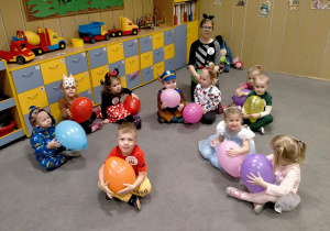 Dzieci i Pani siedzą na dywanie z balonami.