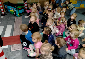 Dzieci siedzą na dywanie i oczekują na wizytę Straży Miejskiej.