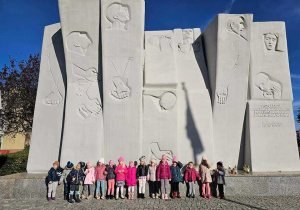 dzieci pozują pod pomnikiem "100 straconych"
