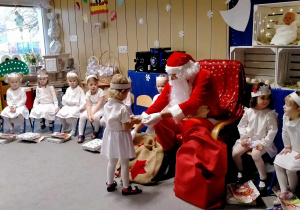 Św. Mikołaj wręcza dziewczynce prezent.