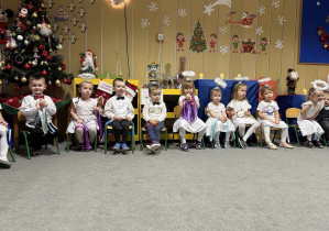 dzieci siedzące na krzesełkach na tle świątecznej dekoracji