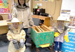 Dzieci z p. Agatą, stoją w strojach pszczelarza przy malowanym ulu.