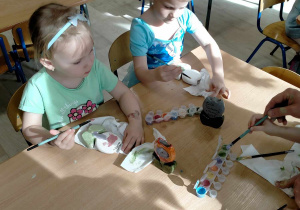 Dziewczynki malują gliniane wazoniki.