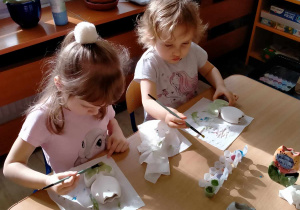 Dziewczynki malują gliniane wazoniki.