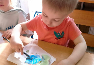 Chłopiec maluje gliniany wazonik.